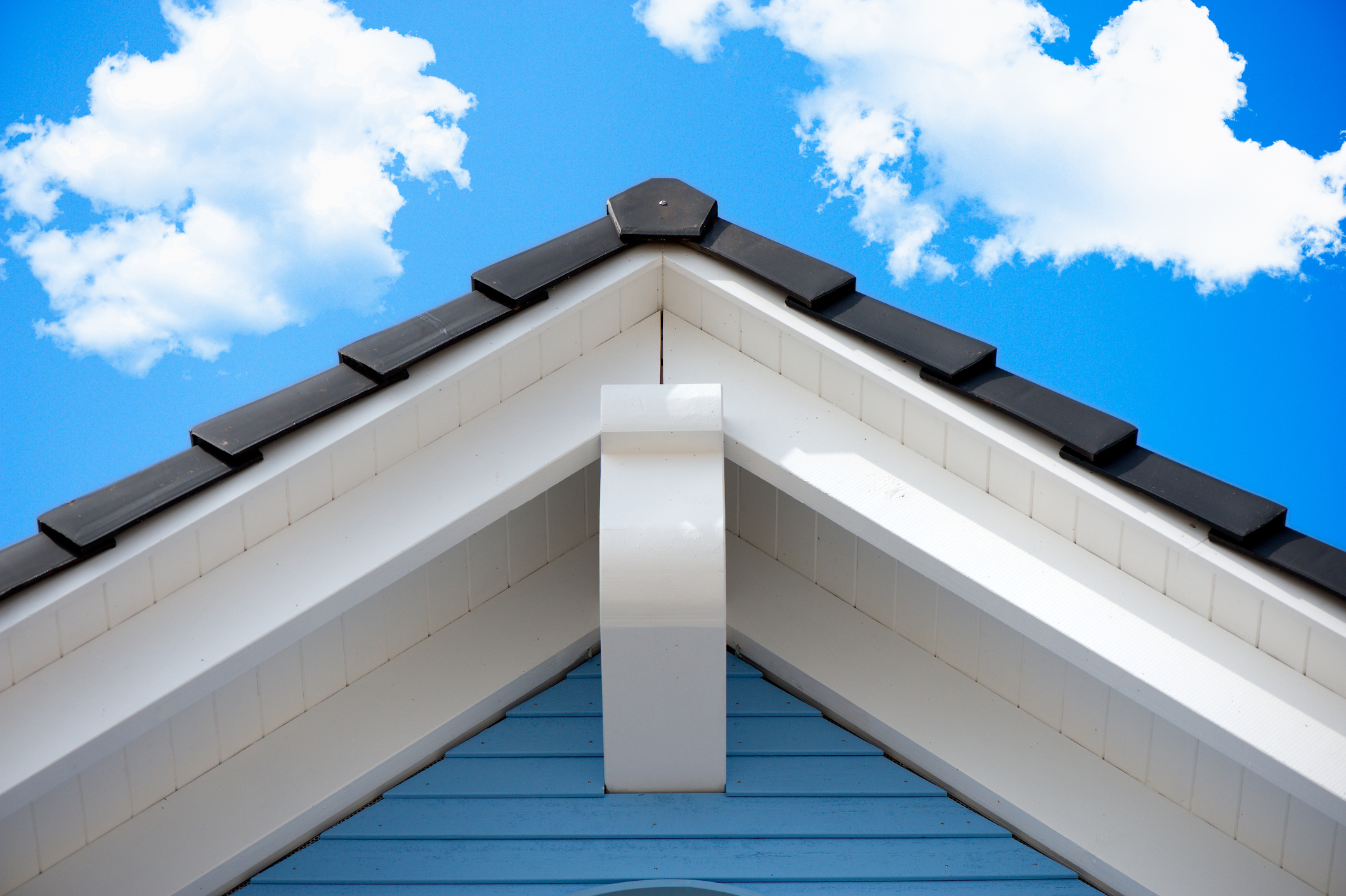 Peak of a residential roof against blue sky